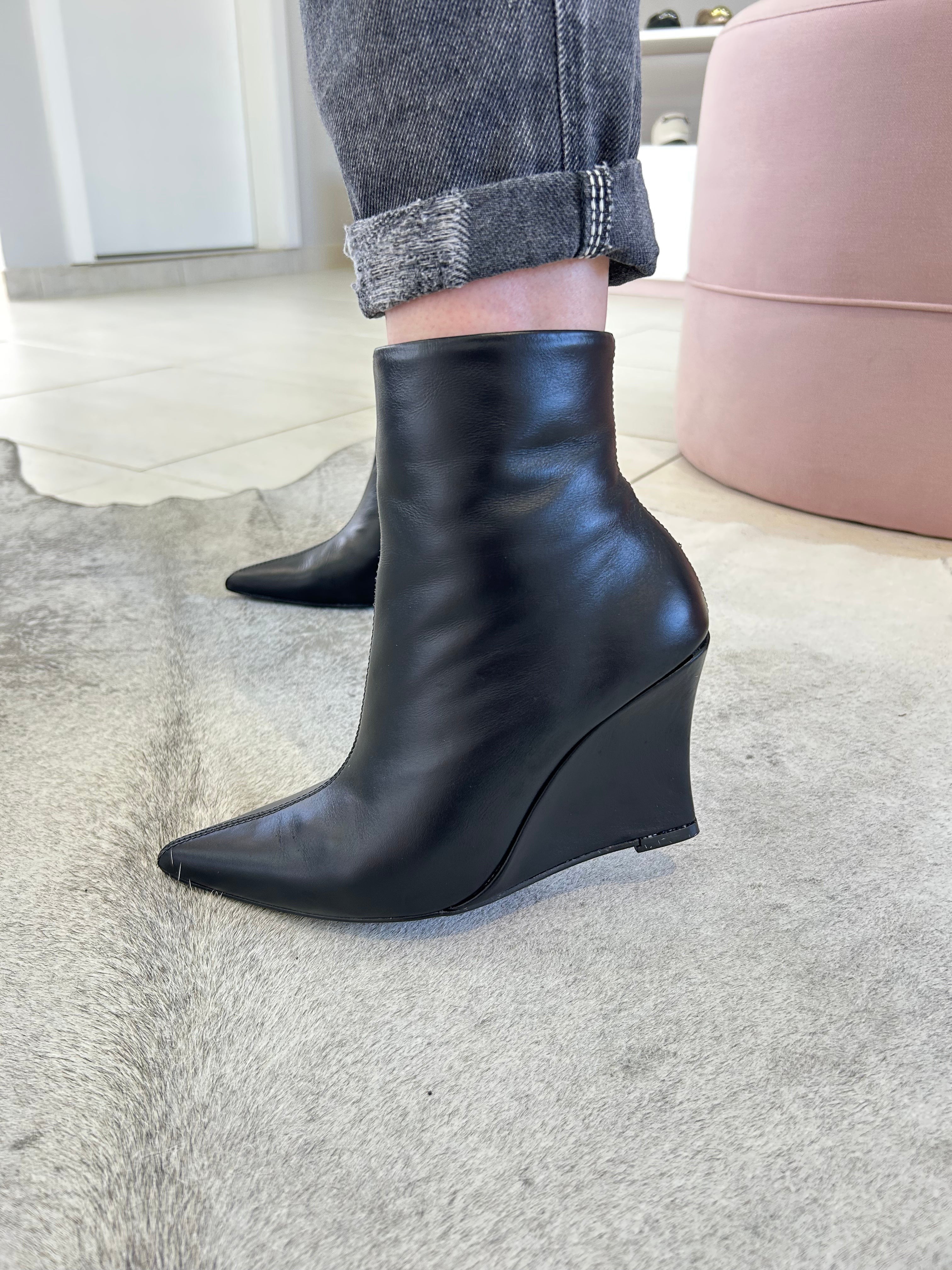 Bota Manchester Beyou Shoes preta em couro com salto anabela e bico fino, usada com calça jeans cinza.