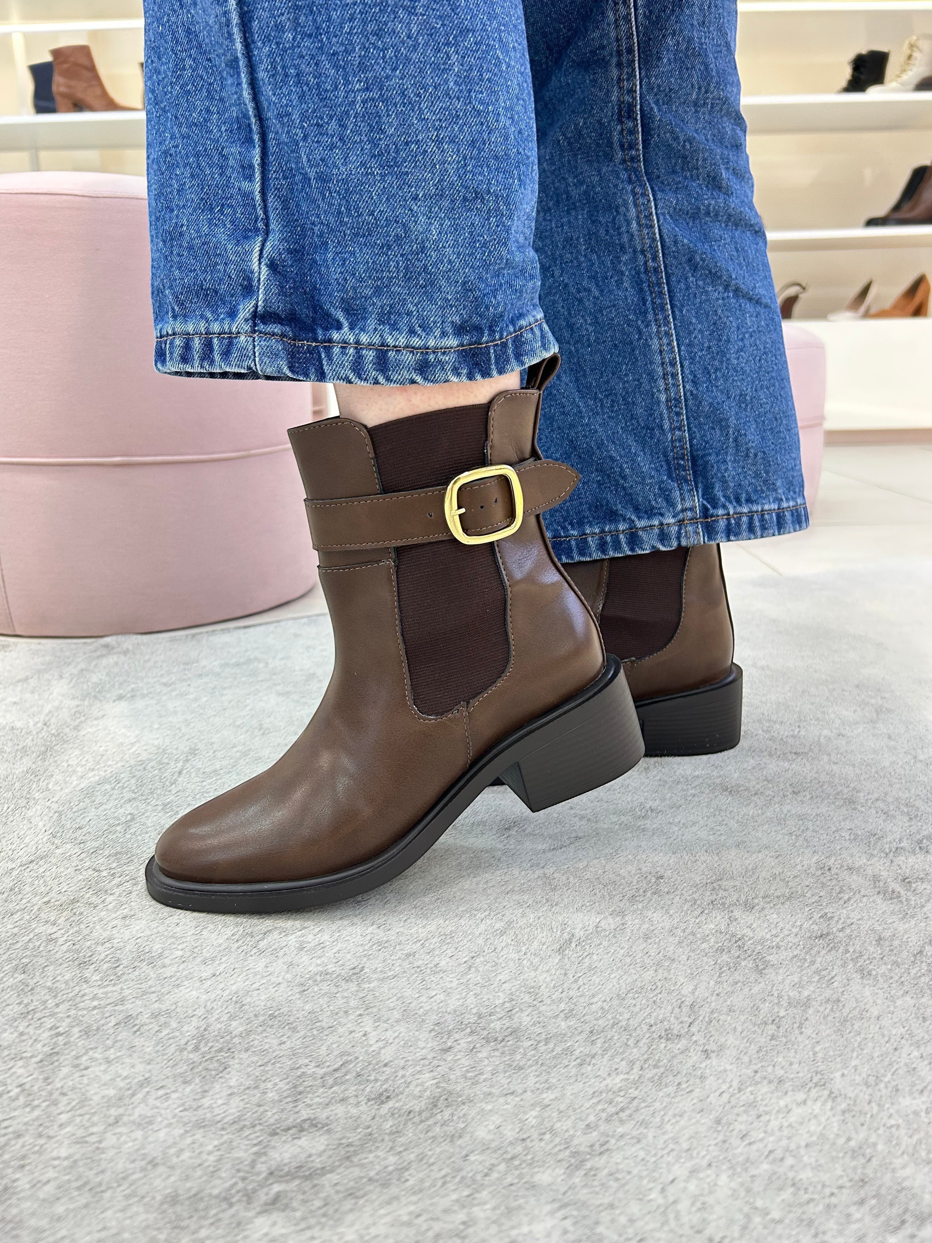Bota Ohio Beyou Shoes marrom em napa destroyed com fivela lateral e elástico, usada com calça jeans azul.