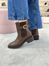 Bota Ohio Beyou Shoes marrom em napa destroyed com fivela lateral e elástico, usada com calça jeans azul.