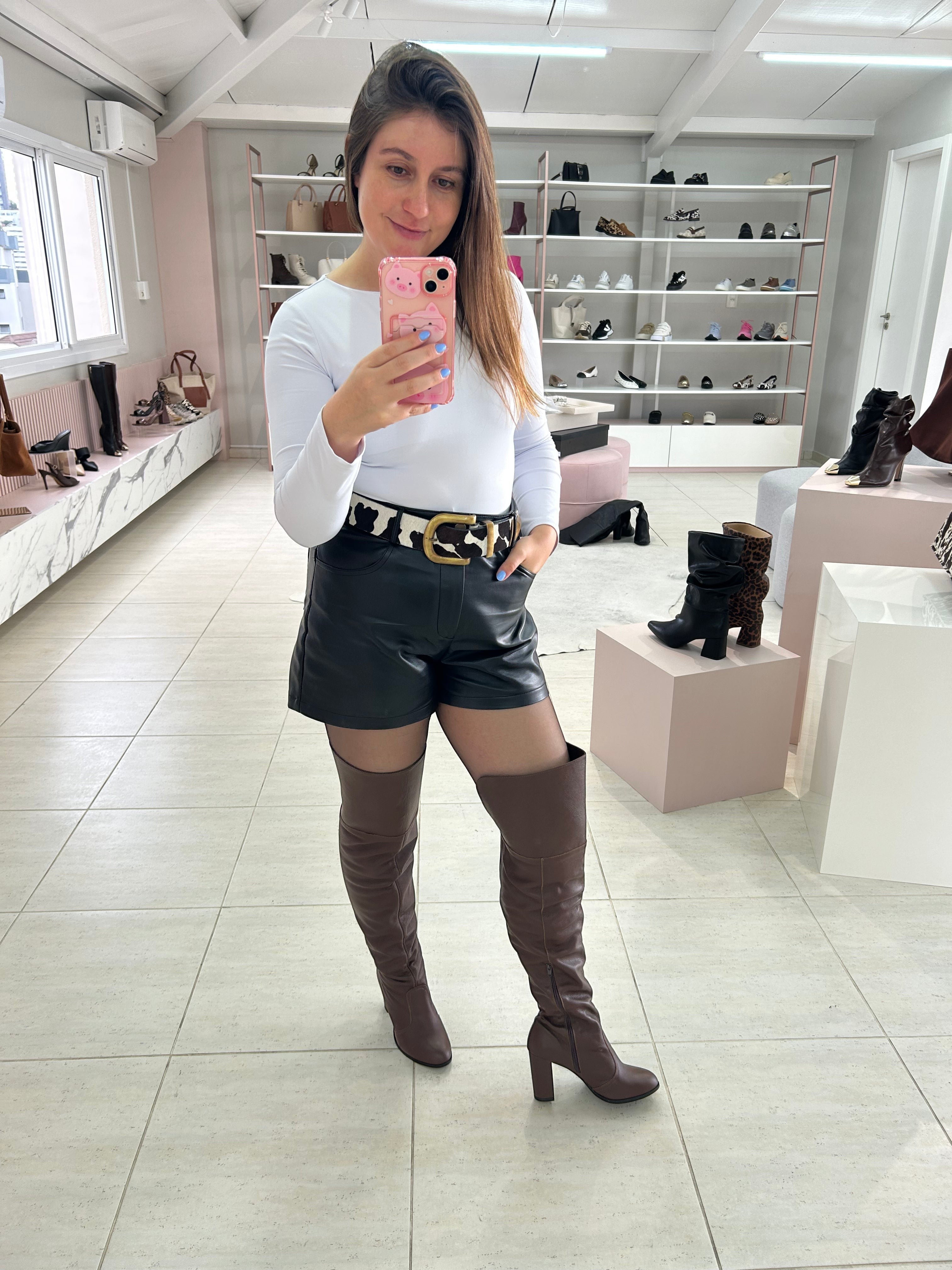 Mulher usando bota over the knee marrom de couro com salto alto da Beyou Shoes em ambiente de loja