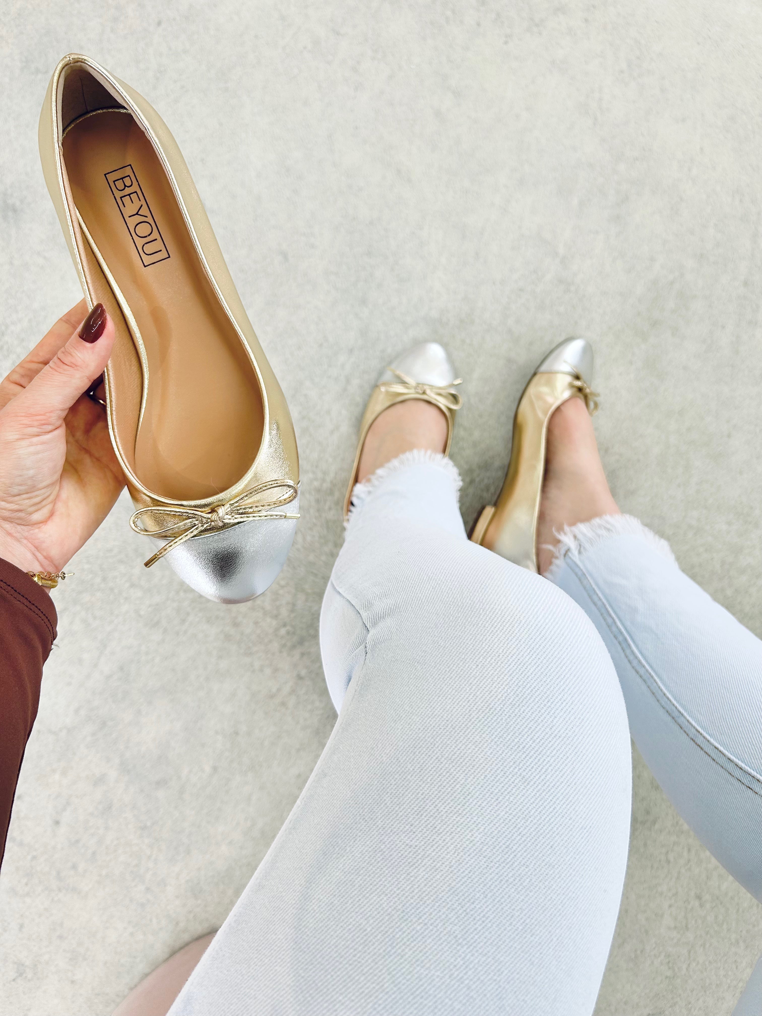 Sapatilha Bari Beyou Shoes em napa ouro light e prata com laço delicado, exibida na mão e nos pés com calça jeans clara.