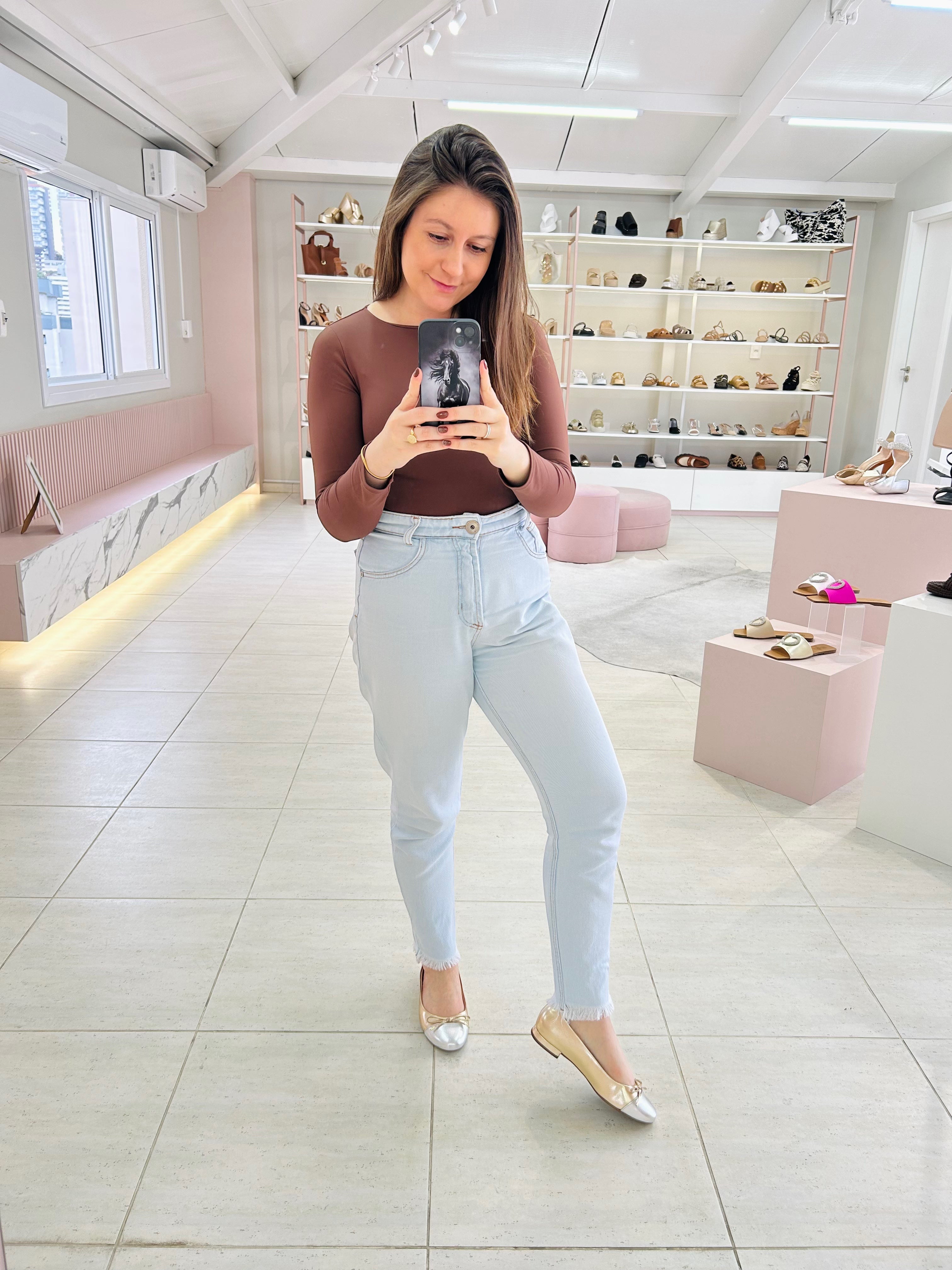 Mulher usando sapatilha Beyou Shoes Bari em napa ouro light e prata em loja de calçados com jeans claro e blusa marrom