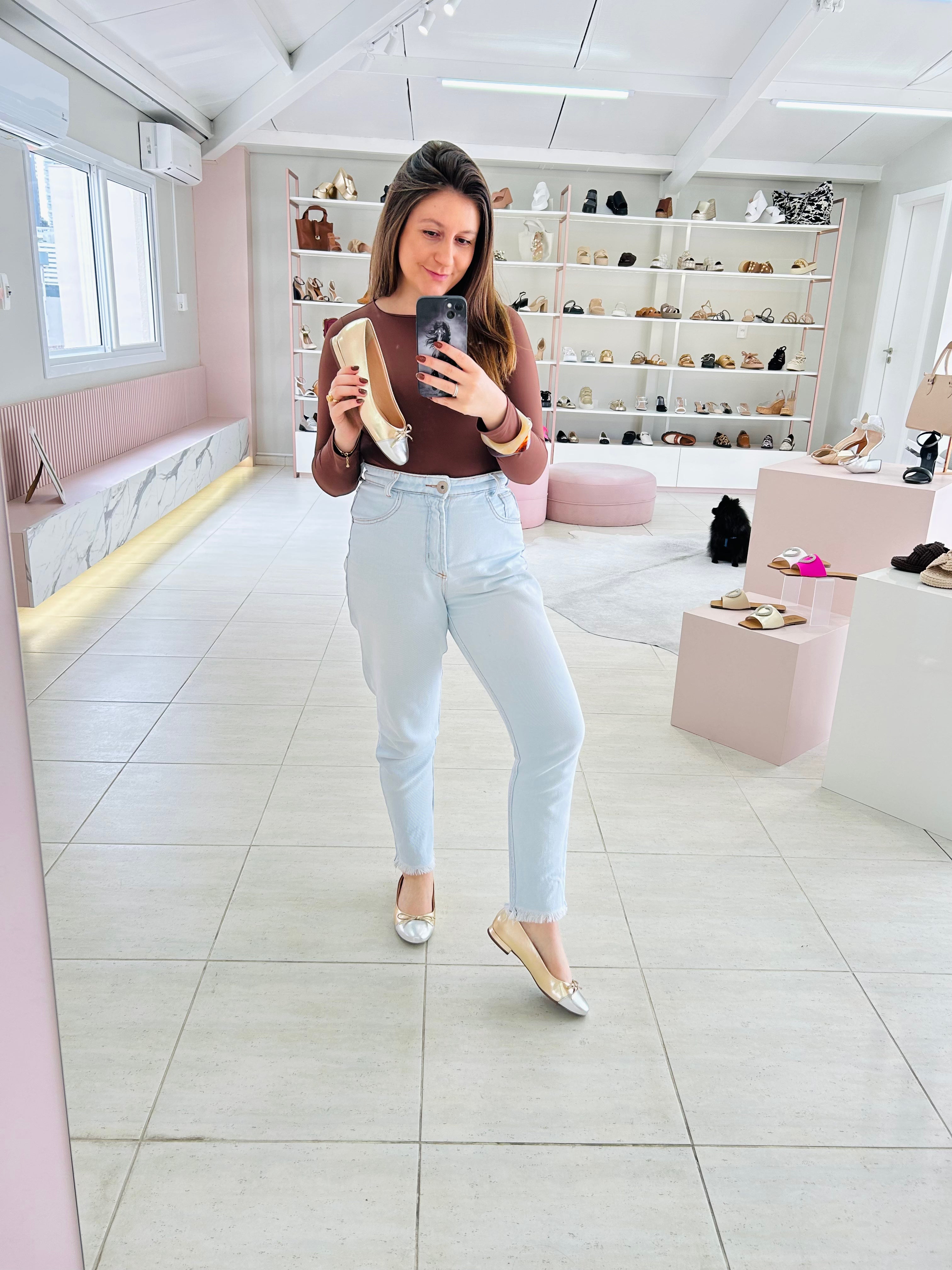 Mulher segurando sapatilha Beyou Shoes Bari em napa ouro light e prata em loja de calçados com espelho