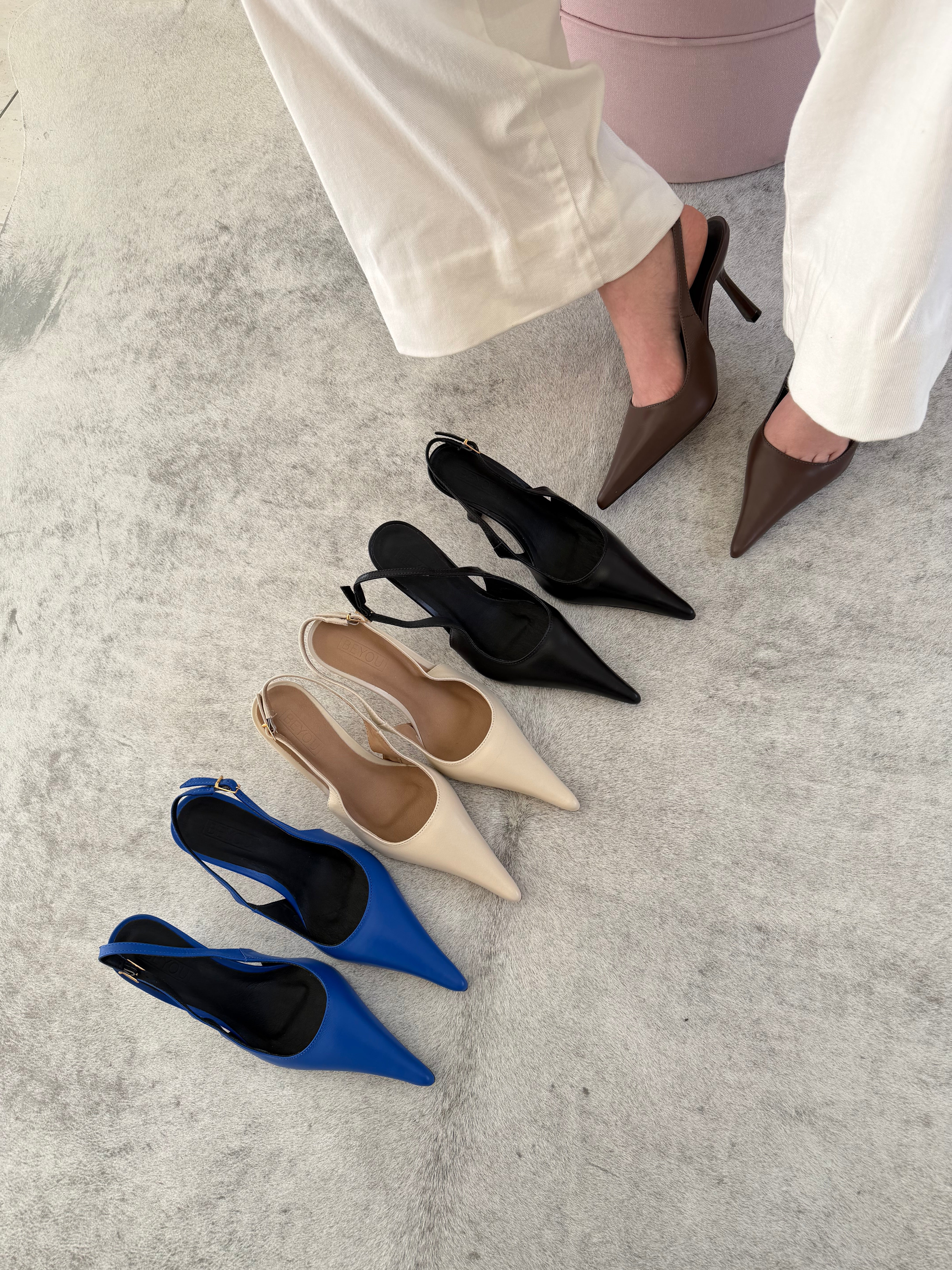 Slingback Beyou Shoes em couro com bico fino e salto taça, disponível em diversas cores sobre tapete cinza.