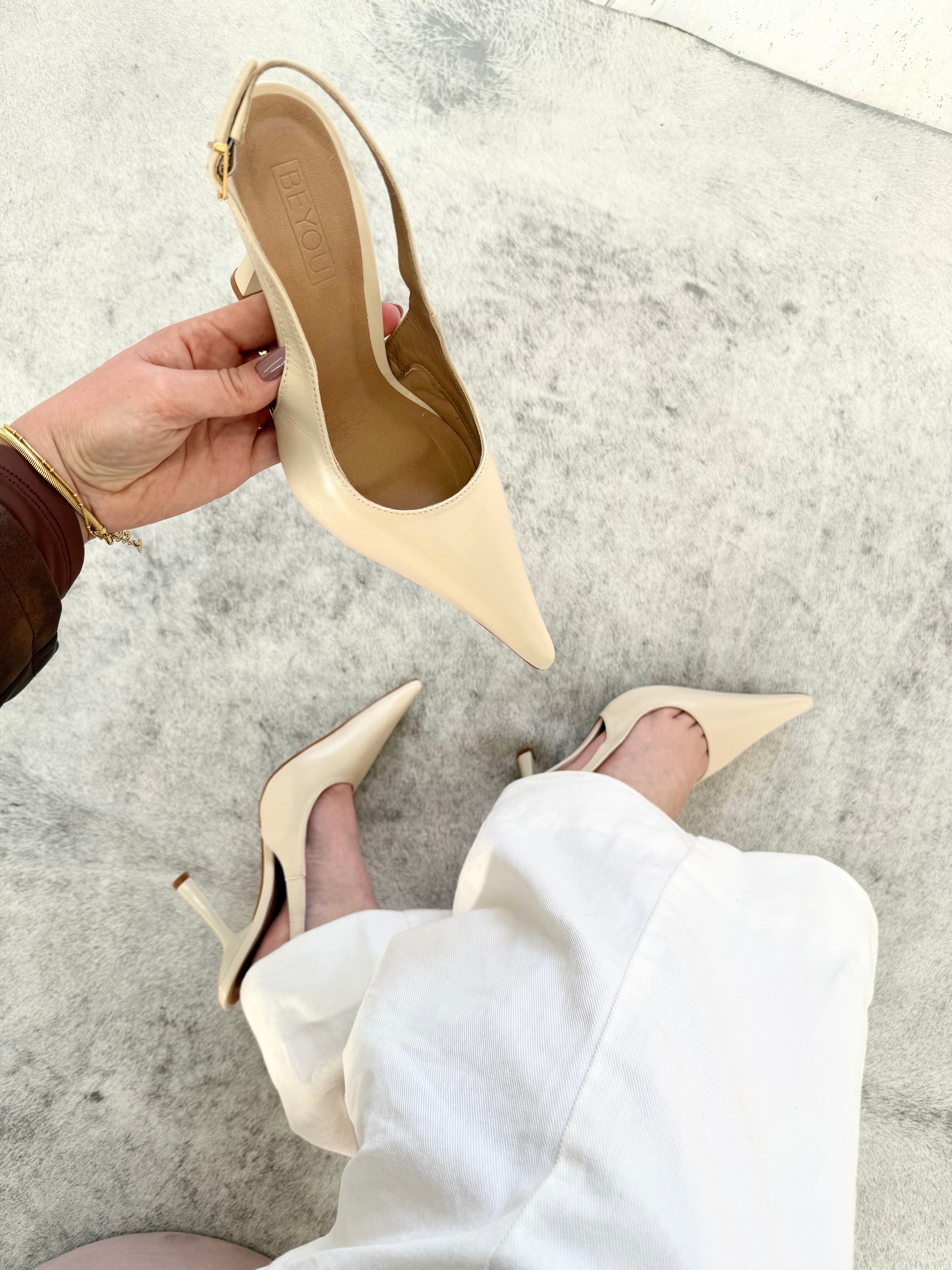 Slingback Beyou Shoes off white em couro com bico fino e salto taça, exibido na mão e calçado