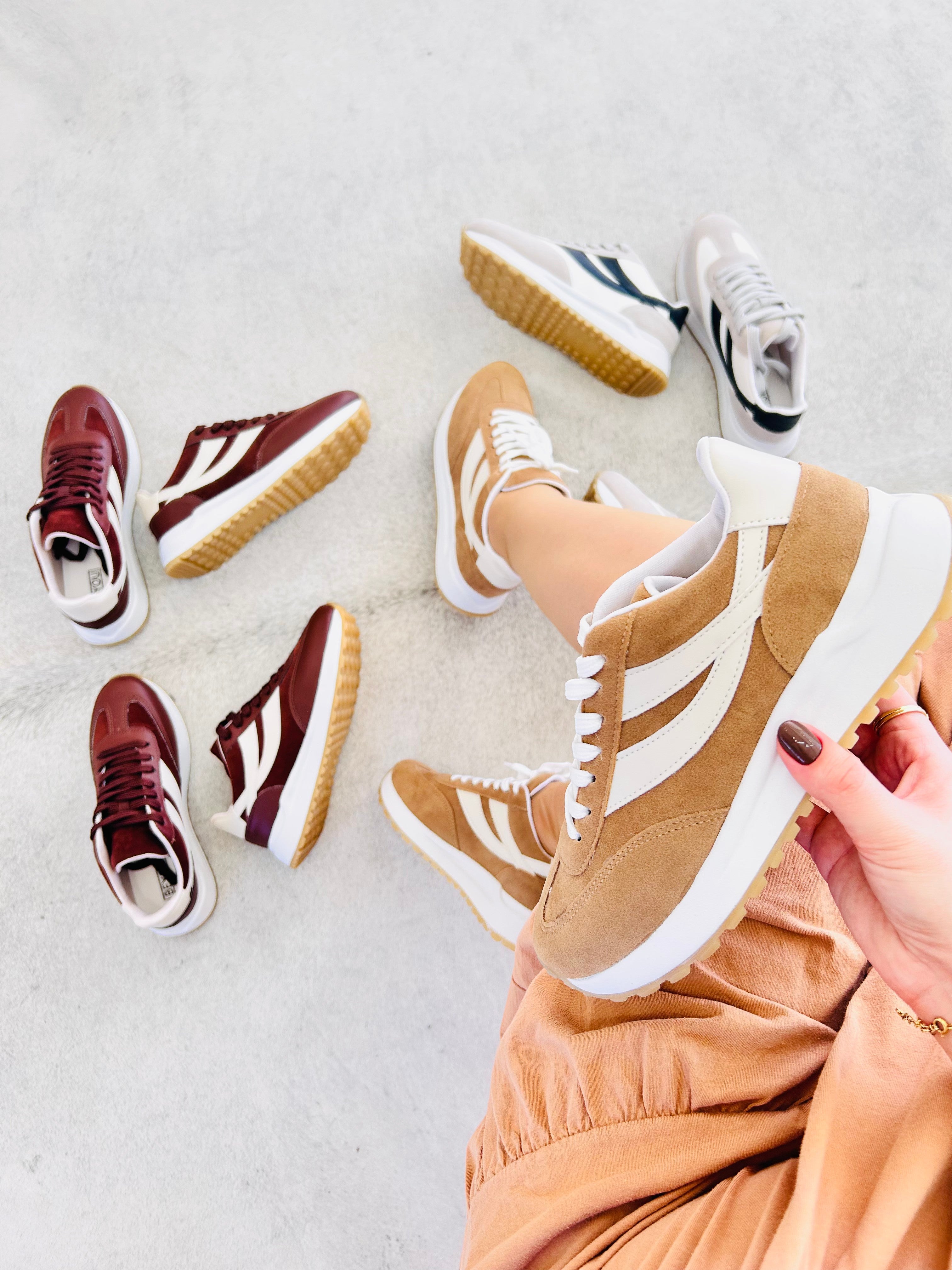 Tênis Oslo Beyou Shoes bege em tecido e camurça sintética, exibido em mão com outros modelos ao fundo.