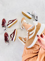 Tênis Oslo Beyou Shoes bege em tecido e camurça sintética, exibido em mão com outros modelos ao fundo.